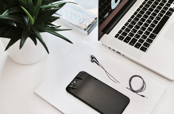 Minimalist workspace with a laptop, smartphone, earphones, and a green plant.