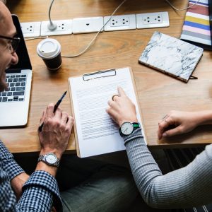 Two people reviewing a document together at a wooden desk with a laptop and coffee.
