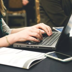 Person typing on a laptop with documents and a smartphone nearby.