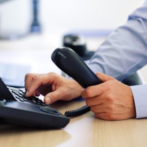 Person dialing on a desk phone while holding the handset.